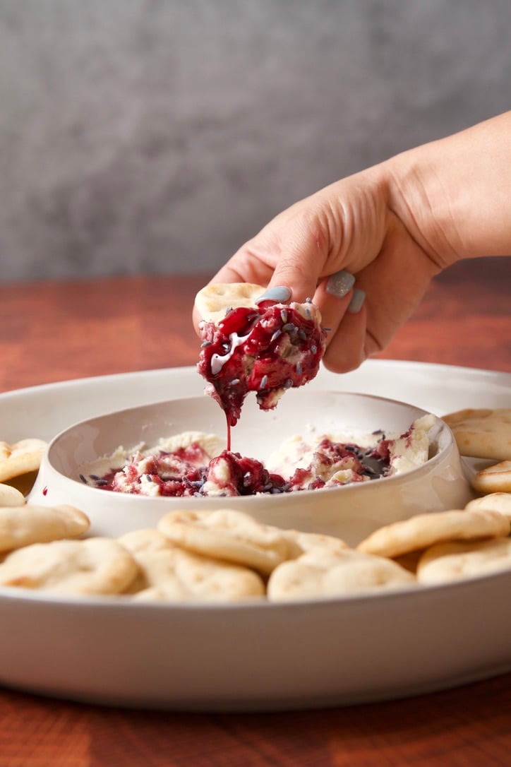 Spooning hibiscus honey over honey and lavender mascarpone dip with snack flats around the bowl