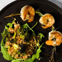 rosemary shrimp skewers with roasted broccoli farro salad on a black plate