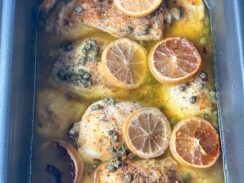 slow cooked chicken piccata in a gray rectangular crockpot topped with lemon rounds and capers