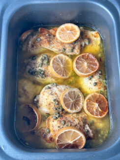 slow cooked chicken piccata in a gray rectangular crockpot topped with lemon rounds and capers