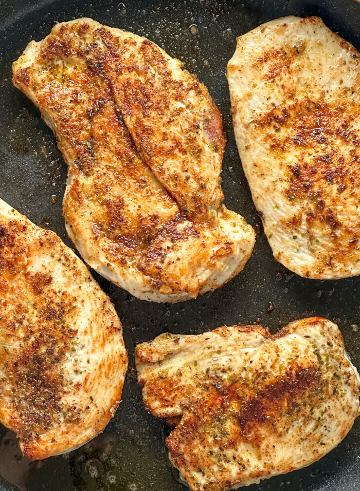 pan seared chicken breasts being cooked at medium heat on a black skillet