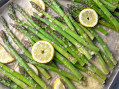 asparagus on a baking sheet with brown parchment with Italian dressing and lemon rounds