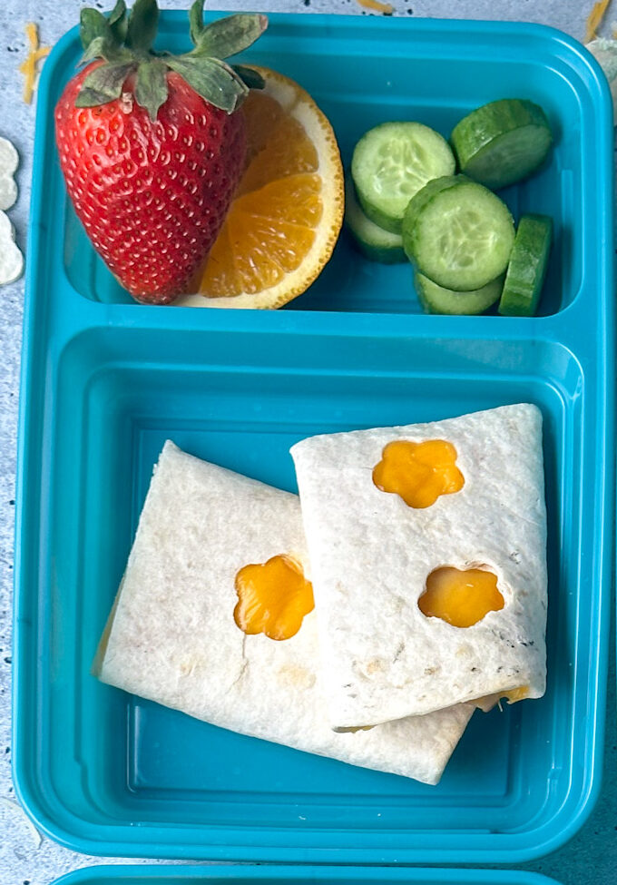 blue lunchbox with cheese quesadilla that has heart stamps on it and served with fresh fruit