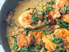 chicken breasts in a black skillet smothered with a dairy free cream sauce, spinach and sun-dried tomatoes