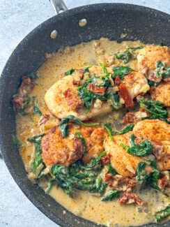 chicken breasts in a black skillet smothered with a dairy free cream sauce, spinach and sun-dried tomatoes