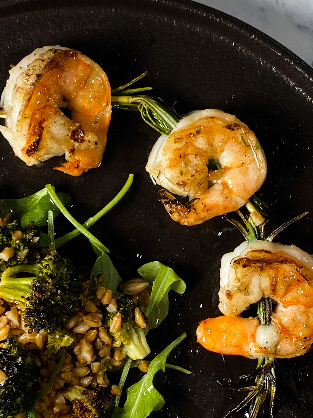 rosemary shrimp skewers with roasted broccoli farro salad on a black plate