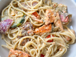 salmon and mediterranean vegetables in a round bowl with creamy spaghetti pasta noodles