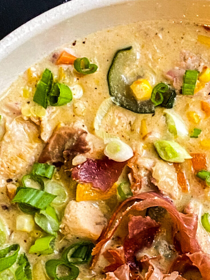 summer veggies and chicken chowder in a bowl topped with prosciutto