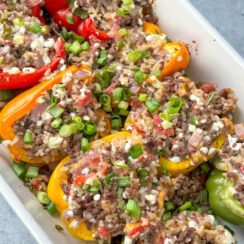 red, orange, yellow, and green stuffed peppers with ground beef, onion, rice, and cottage cheese mixture in a white baking dish topped with green onion