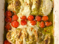 chicken breasts smothered in pesto and mozzarella cheese alongside roasted cherry tomatoes in a baking dish