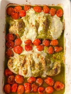 chicken breasts smothered in pesto and mozzarella cheese alongside roasted cherry tomatoes in a baking dish