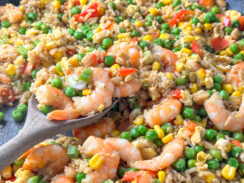 shrimp, rice, peas, carrots, corn, and scrambled eggs on a wooden spoon in a large black skillet