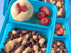 cheesy black bean chili topped with queso and served with a heart shaped corn dog muffin and fruit in a blue lunchbox container.
