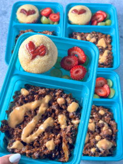 cheesy black bean chili topped with queso and served with a heart shaped corn dog muffin and fruit in a blue lunchbox container.