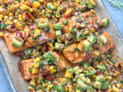 salmon fillets on a sheet pan with roasted corn and topped with peach avocado salsa