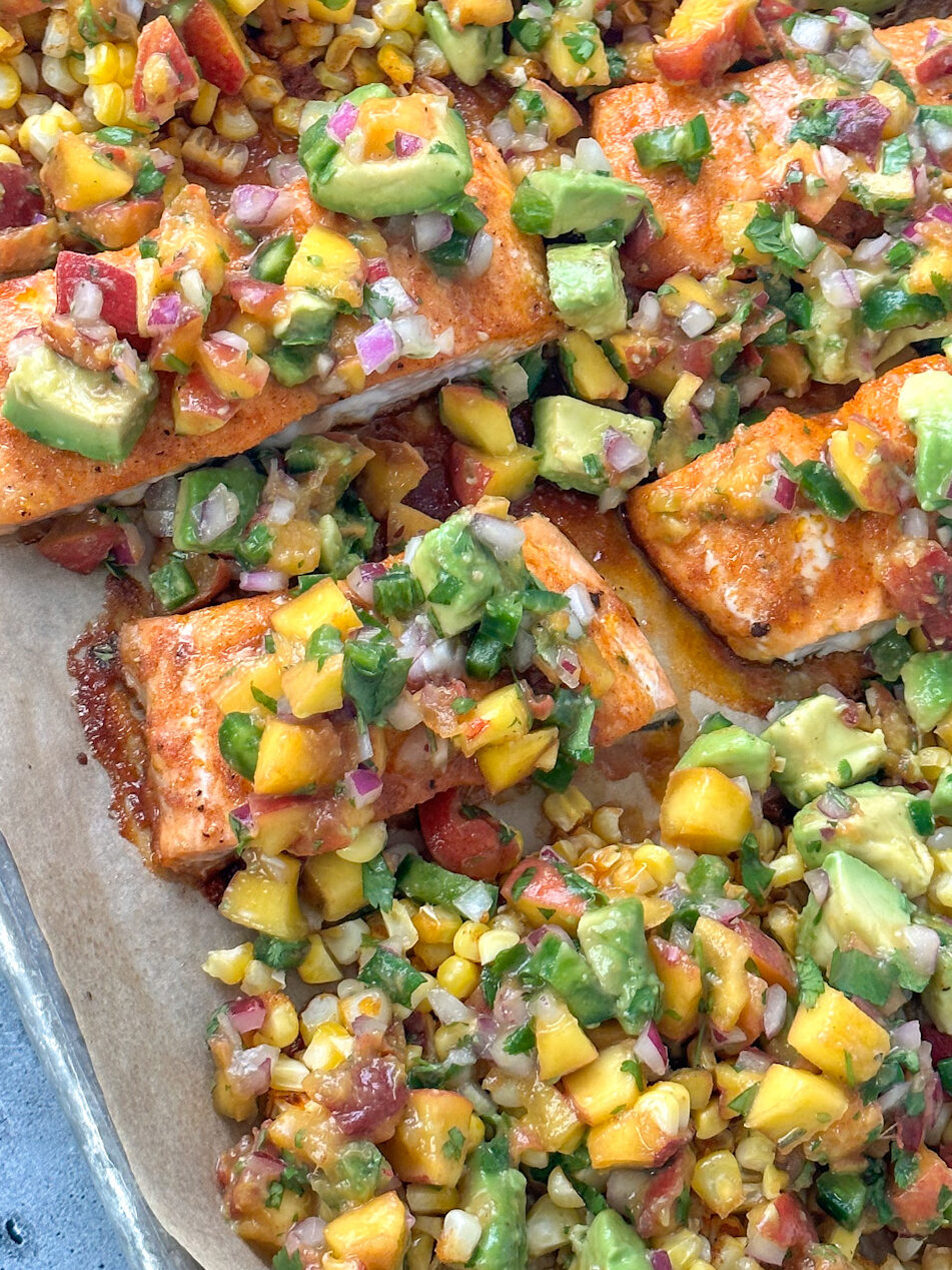 salmon fillets on a sheet pan with roasted corn and topped with peach avocado salsa