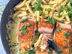 Seared salmon in a large skillet with a pesto cream sauce and penne pasta
