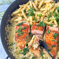 Seared salmon in a large skillet with a pesto cream sauce and penne pasta