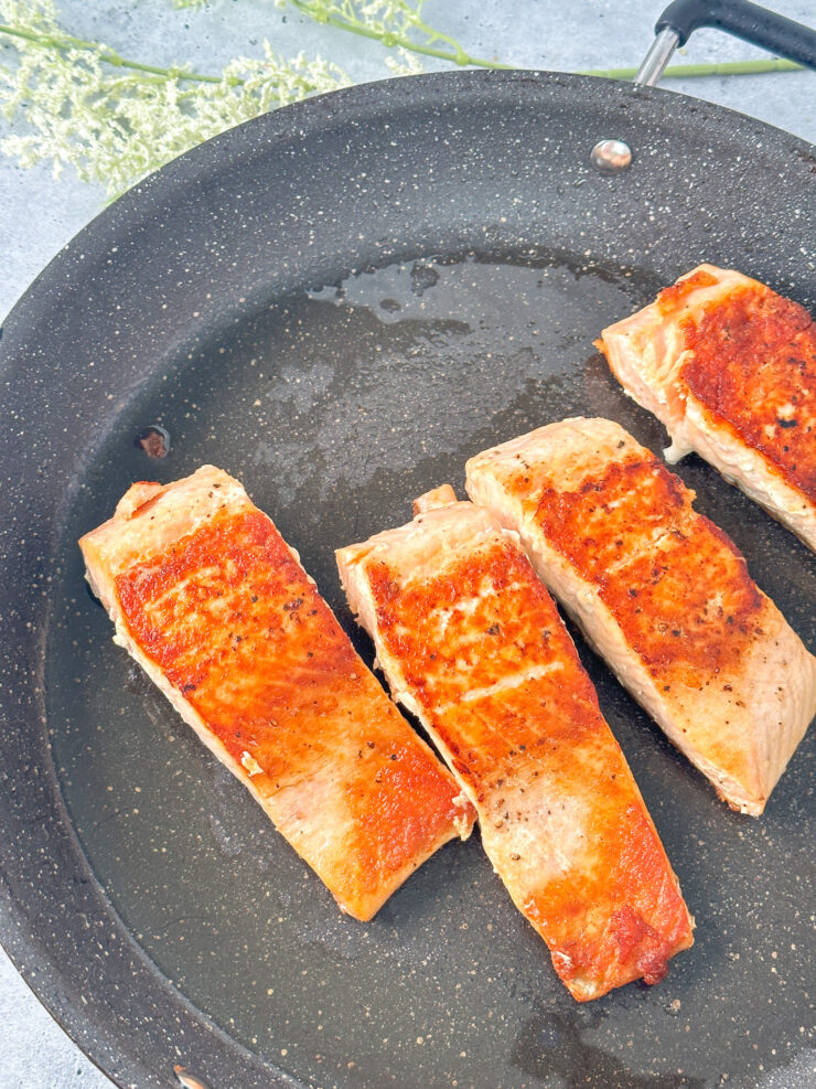 four crispy salmon filets in a larger black skillet