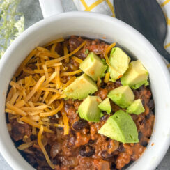 black bean chili served in a white bowl with cheddar cheese and fresh avocado