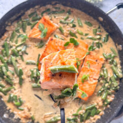 crispy salmon on a fork with a creamy garlic green bean sauce in a large black skillet