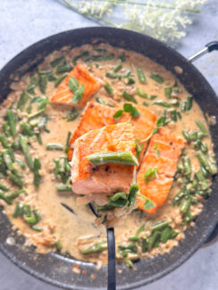 crispy salmon on a fork with a creamy garlic green bean sauce in a large black skillet