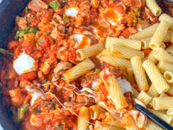 rigatoni pasta in a black skillet topped with chicken, vegetables, marinara sauce and fresh mozzarella cheese.