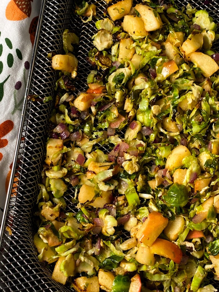 roasted shredded brussel sprouts on a air fryer pan with diced apples, red onion, and maple syrup glaze.