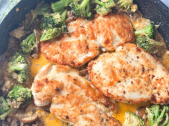 3 pan seared thin chicken breasts in a black skillet with a creamy garlic sauce and mushrooms and broccoli