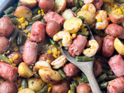 cooked shrimp, sausage, green beans, potatoes, corn and lemon wedges on a sheet pan with a wooden spoon