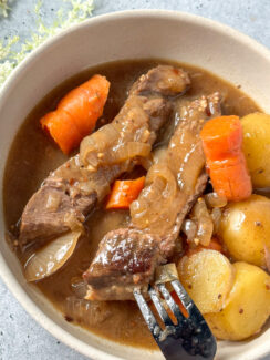 London broil pot roast with a garlic onion brown gravy, with potatoes and carrots, and onion in a white bowl with a black fork