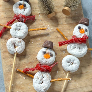 3 powdered donuts on wooden skewers decorated like snowmen