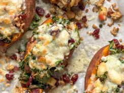 stuffed sweet potatoes on a baking sheet with kale, cranberries, crumbled sausage, and melted pepper jack cheese.