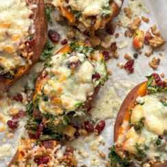 stuffed sweet potatoes on a baking sheet with kale, cranberries, crumbled sausage, and melted pepper jack cheese.