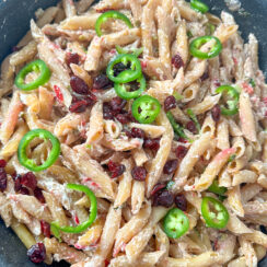 penne pasta in a creamy sauce topped with sliced jalapeños and cranberries in a black skillet