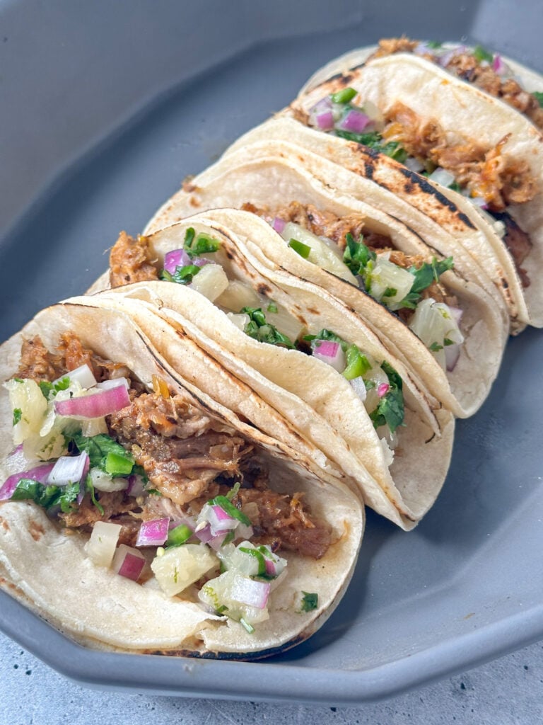 charred corn tortillas with seasoned pulled pork and pineapple cilantro salsa inside in a gray serving platter