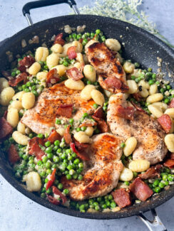 pan seared chicken in a black skillet with peas, bacon, and gnocchi