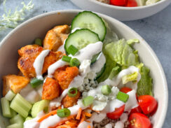 buffalo chicken, lettuce, cucumbers, cherry tomatoes, quinoa, shredded carrots, sweet potato puffs in a white bowl with ranch dressing