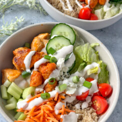buffalo chicken, lettuce, cucumbers, cherry tomatoes, quinoa, shredded carrots, sweet potato puffs in a white bowl with ranch dressing