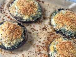 large portobello mushrooms on a baking sheet with parchment paper stuffed with spinach, boursin cheese and topped with crispy breadcrumbs.