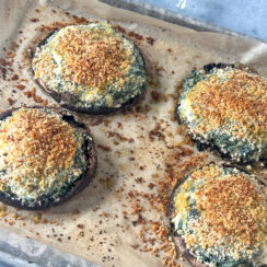 large portobello mushrooms on a baking sheet with parchment paper stuffed with spinach, boursin cheese and topped with crispy breadcrumbs.