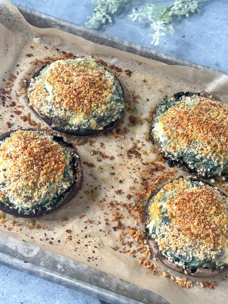Four stuffed portobello mushrooms with golden parmesan panko topping on a parchment-lined baking sheet