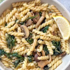 pasta with spinach, mushrooms, and a lemon wedge in a white bowl