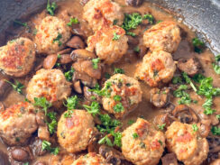 baked meatballs in a black skillet with mushrooms in a creamy marsala sauce and topped with fresh parsely leaves