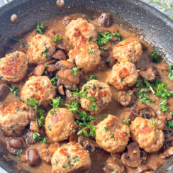 baked meatballs in a black skillet with mushrooms in a creamy marsala sauce and topped with fresh parsely leaves