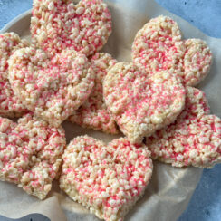 heart shaped Rice Krispie treats with pink sprinkles on a plate with parchment paper