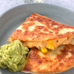 crispy quesadillas cut into wedges with a cheesy taco dip filling served with guacamole on a gray plate