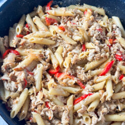 thinly sliced chicken breast with caramelized onions and peppers, melted American cheese and penne pasta in a large black skillet