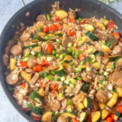 sliced chicken sausage, zucchini, cherry tomatoes, and rice with a stir-fry sauce in a large black skillet