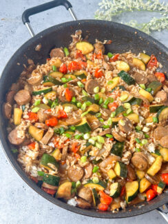 sliced chicken sausage, zucchini, cherry tomatoes, and rice with a stir-fry sauce in a large black skillet